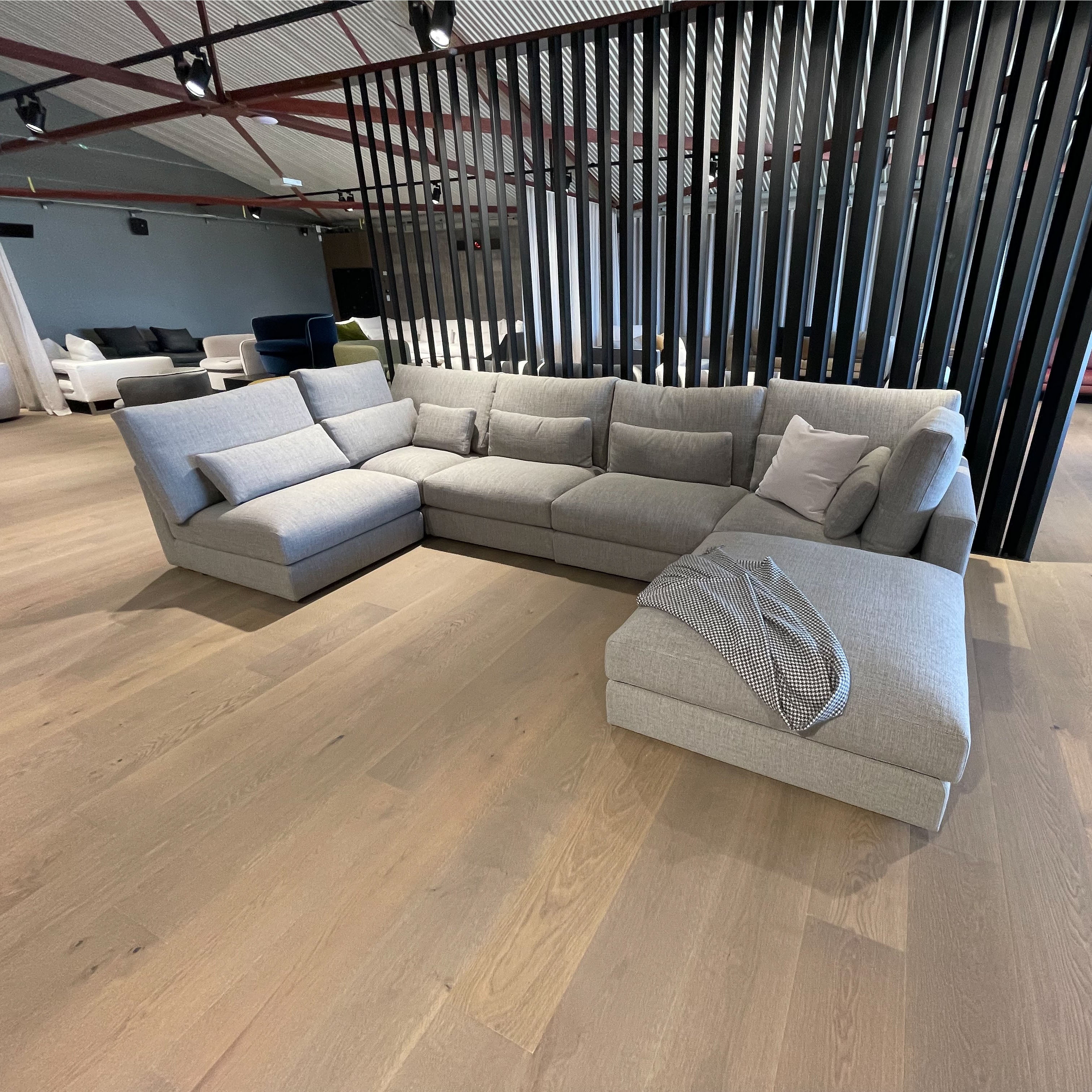 Gray sectional sofa in a modern indoor setting with wooden flooring and black metal screen.