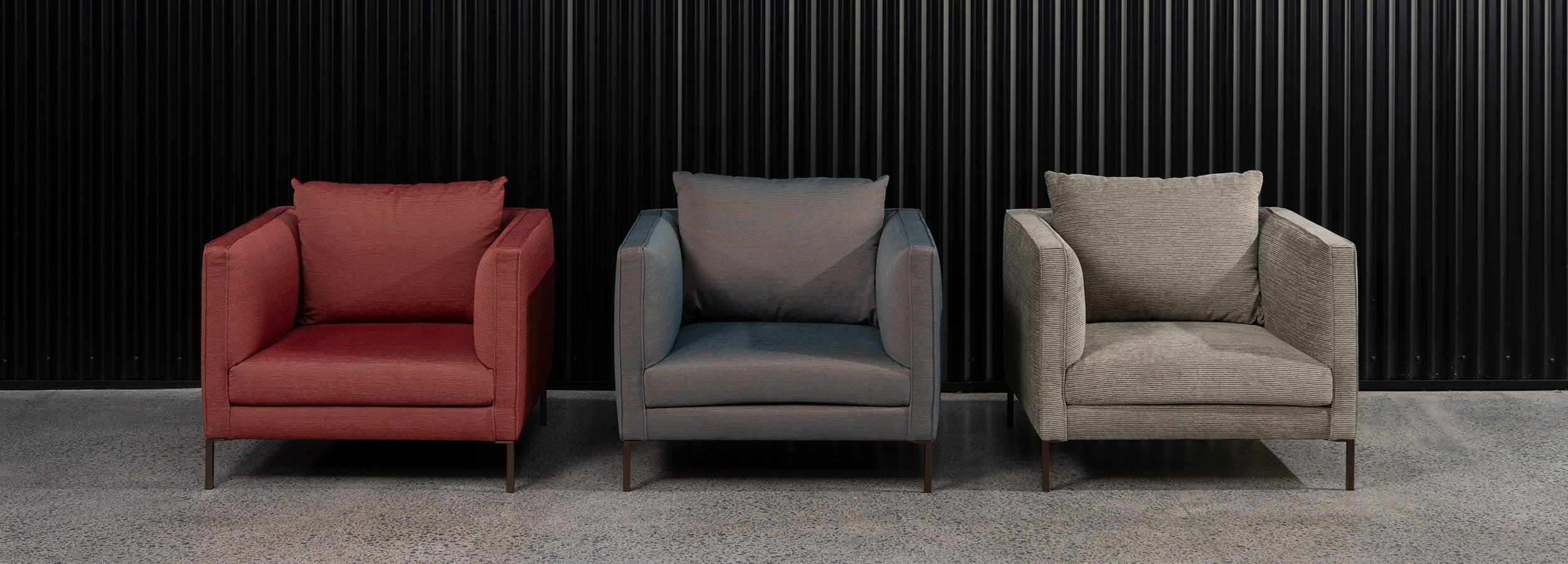 Three Italian made Siena armchairs in a row in a showroom setting with dark black wall as backdrop.