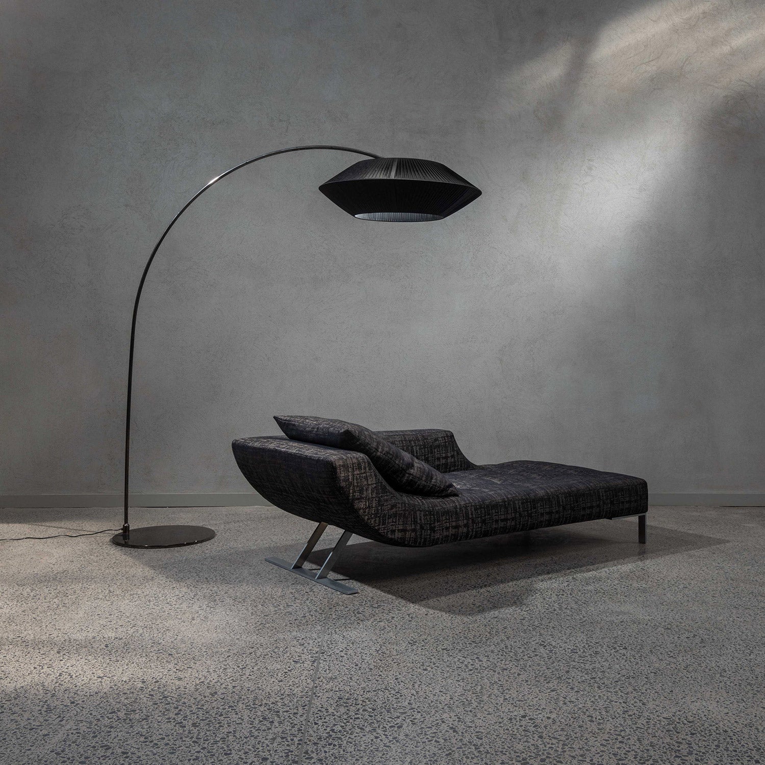 Viceversa chaise longue in black and grey tone fabric on showroom floor with an Arte Arc floor lamp in black over it.