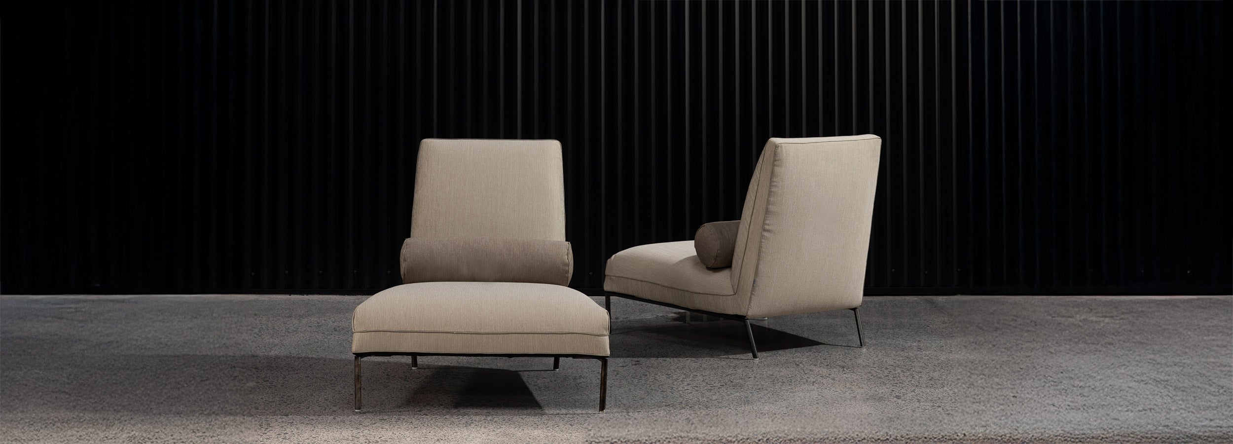 Two Nomade lounge chairs. One facing forward, the other showing the back in an angle with dark walled showroom background.